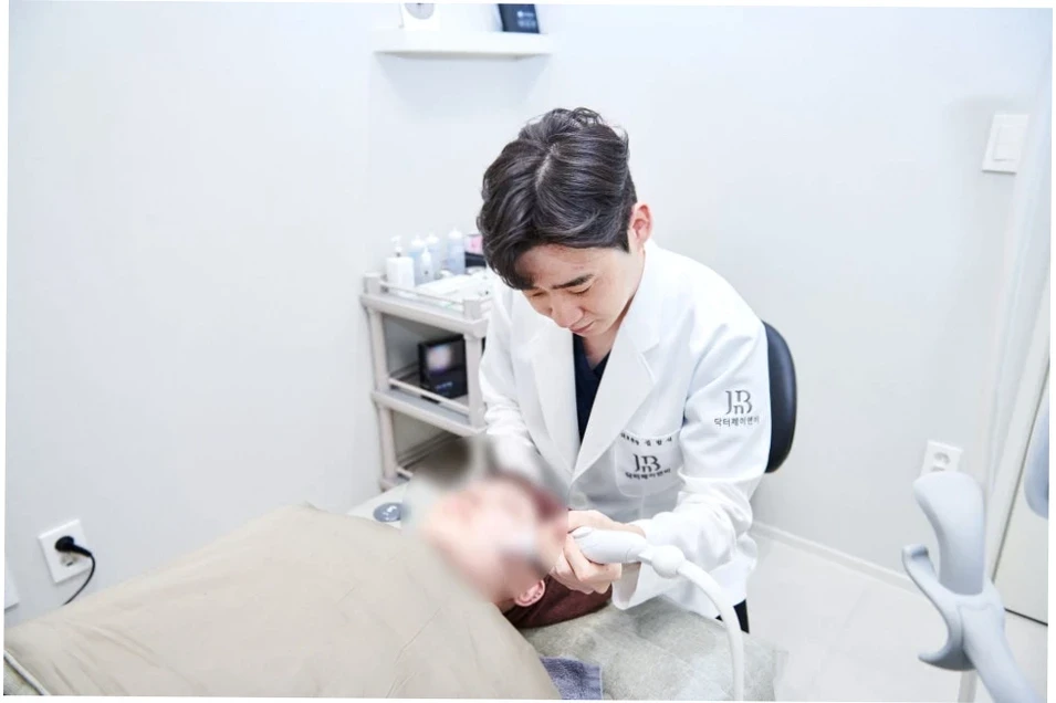 흰색 가운을 입은 의사가 베드에 누워 있는 환자의 얼굴에 의료기기를 이용해 시술하는 모습. 시술 전후 느껴지는 울쎄라 300샷 600샷 차이 비교를 돕는 시술 장면.